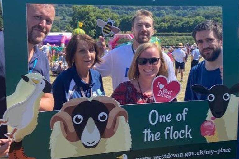 A photograph of staff at the Okehampton show. They are posing behind a selfie frame that says "One of the flock" and has a cartoon image of a Dartmoor sheep. The five staff members are smiling and enjoying the sunshine!