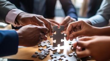 A group of hands, working together to solve a jigsaw on a table.