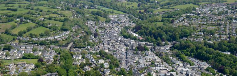 An aerial view of Tavistock, showing the town on a sunny day, nestled in green fields with Dartmoor visible in the distance.