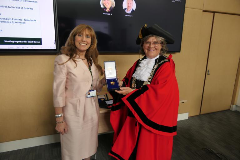 A photo of councillors Debo Sellis, the new mayor of West Devon, dressed in the West Devon mayoral regalia, presenting a pendant to councillor Lynn Daniel.