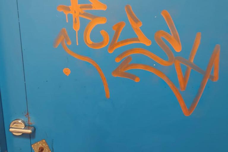 An example of vandalism in our public toilets - an orange graffiti tag sprayed on the blue door of the toilets.