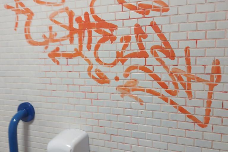 An example of vandalism in our public toilets - an orange graffiti tag sprayed on the wall of the toilets.