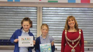 Cllr Lynn Daniel standing next to two children holding a certificate and book