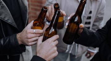 Arms and bodies of people clinking brown beer bottles together on the street ready to take a drink